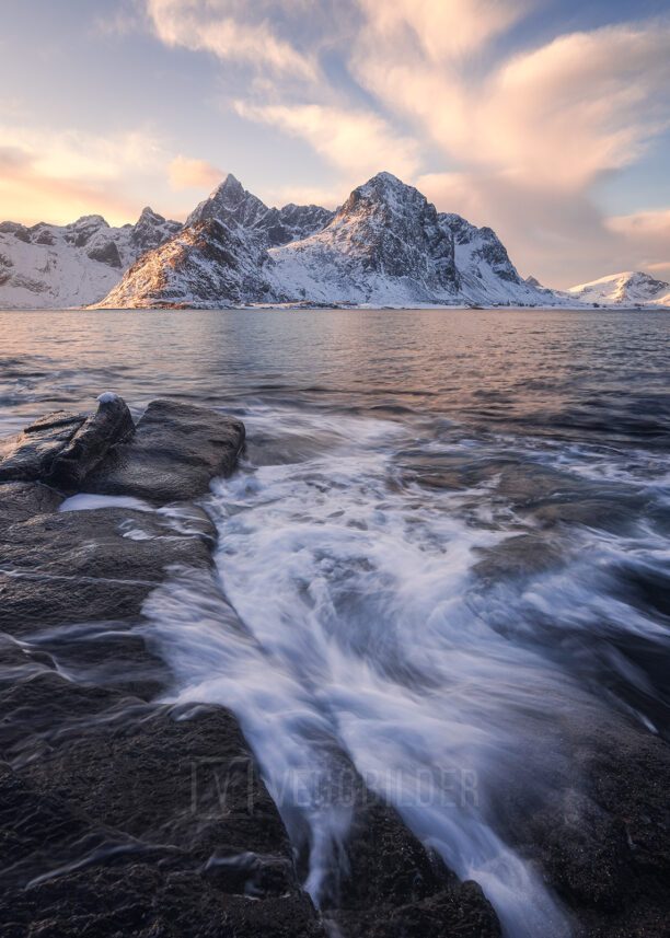 Bølger som slår inn mot land i forgrunnen og snødekte fjell i bakgrunnen., fotokunst veggbilde / plakat av Klaus Axelsen
